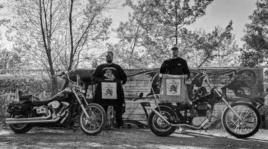 Two club members standing with choppers in front of a painted wall